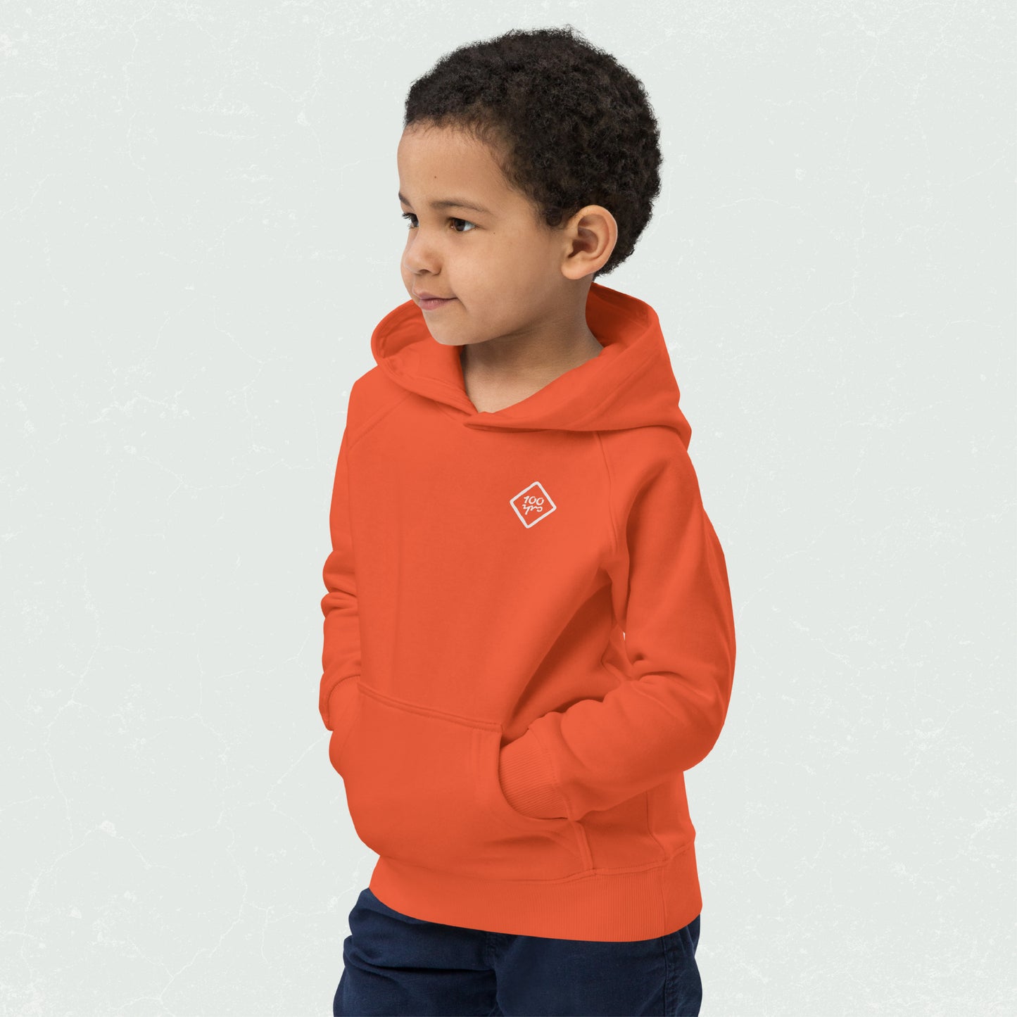 Child wearing an orange hoodie with 100yrs logo, featuring front pouch pocket and jersey-lined hood.