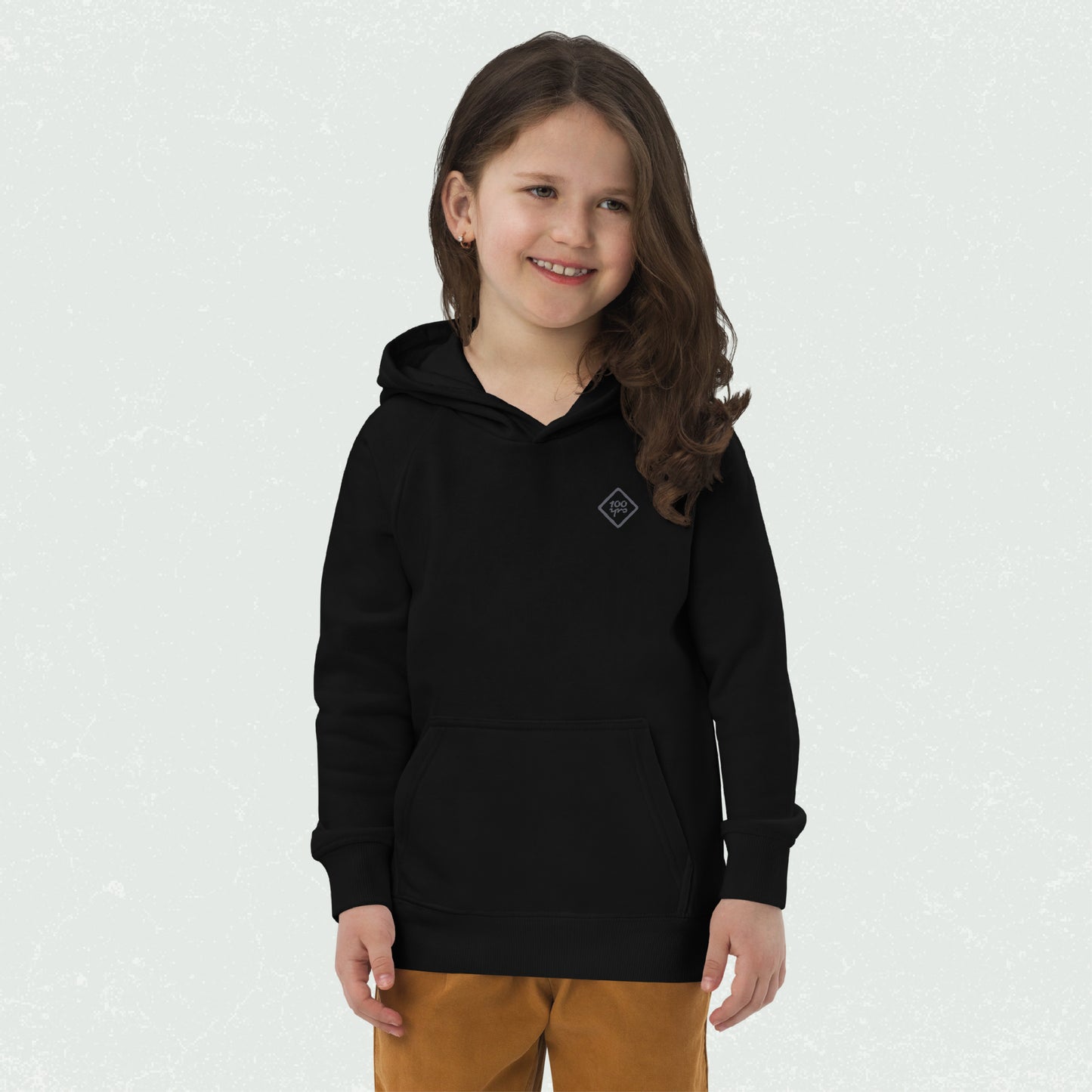 A child wearing a black unisex eco hoodie with a 100yrs logo on the chest, paired with brown pants.