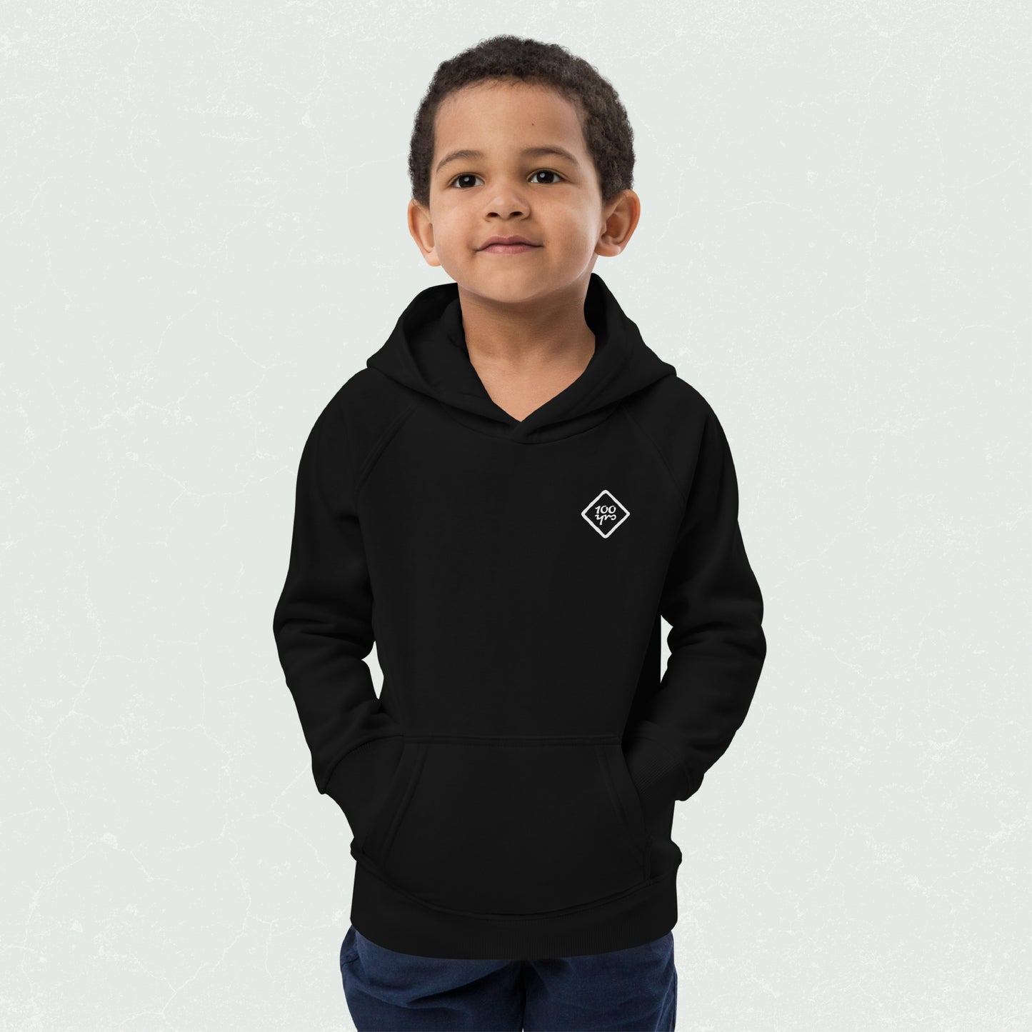 Kid wearing a black eco-friendly hoodie with "100yrs" logo in diamond shape, hands in front pouch pocket, and a comfortable fit.