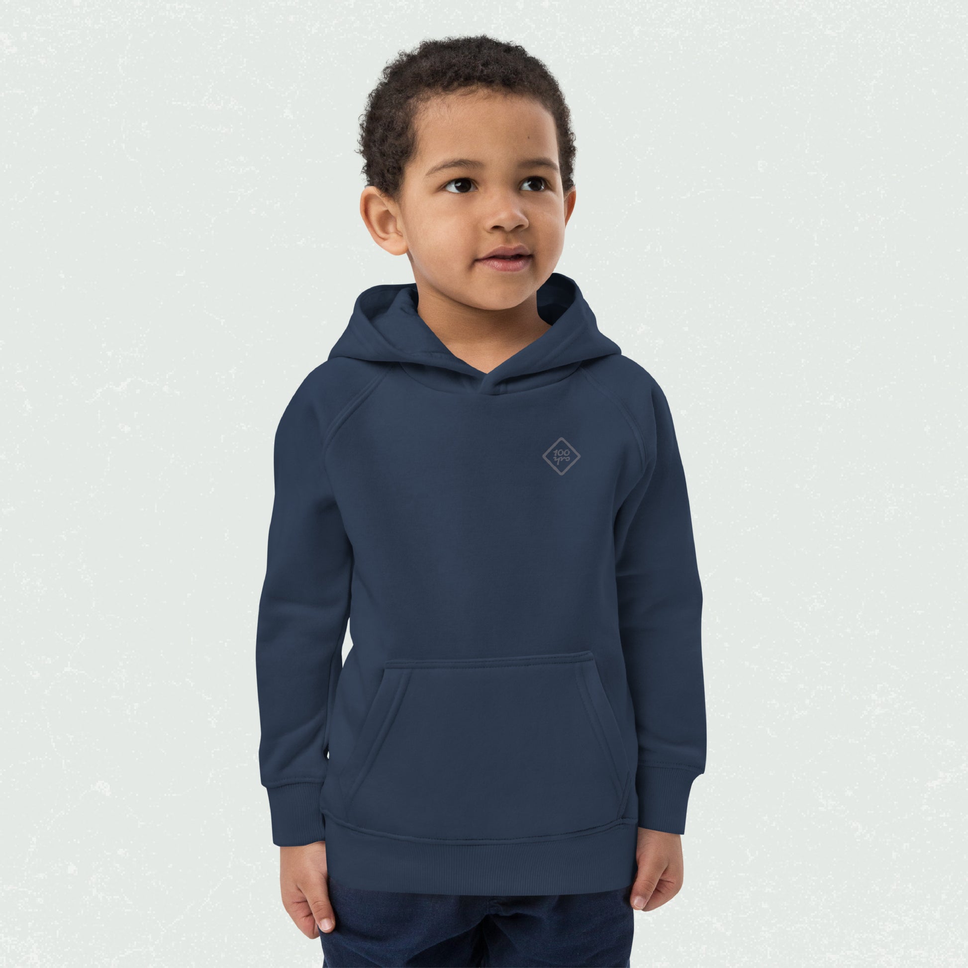 Young child wearing the Unisex Kids Eco Hoodie in navy blue featuring the 100yrs logo, with a relaxed fit and front pouch pocket.